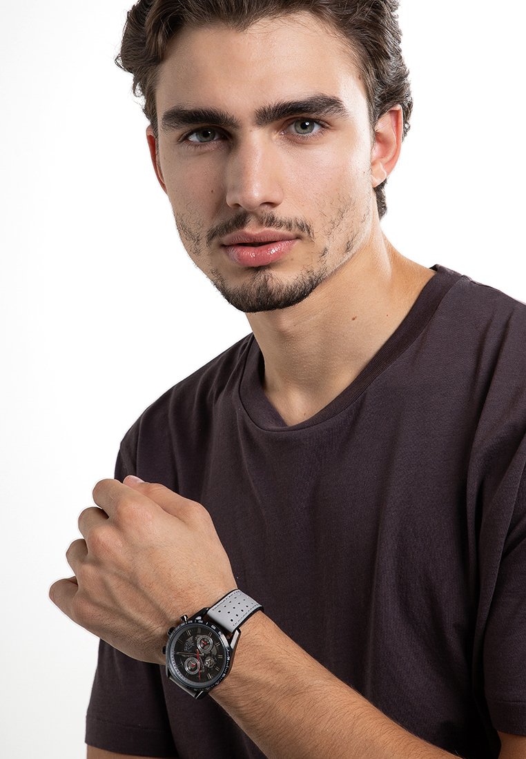 Montre analogique avec un cadran noir, des accents argentés et un bracelet perforé gris. Boîtier rond avec trois sous-cadrans et une finition polie.