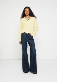 Polo jaune clair à manches longues avec trois boutons, associé à un jean évasé bleu foncé. Le jean présente un design classique à cinq poches.