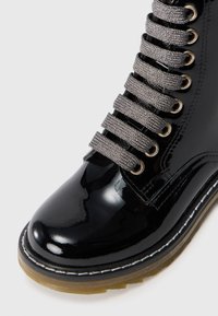 Bottines en cuir verni noir avec un bout arrondi, dotées de lacets gris métalliques, d'œillets dorés et d'une semelle épaisse et texturée.