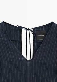 Encolure de vêtement bleu marine à fines rayures avec une découpe en V et des liens fins dans le dos, révélant une étiquette noire Massimo Dutti à l’intérieur.