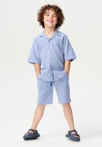Ensemble de chemise à manches courtes et de shorts à carreaux bleus et blancs avec des boutons, comprenant des poches avant. Porté avec des sandales navy.