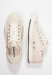 Sneakers in pelle beige con lacci, zip laterale e accento nero sulla suola. Presentano occhielli in metallo e una finitura testurizzata.