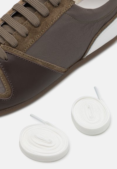 Baskets en suede et cuir marron avec des surfaces texturées, accents gris et panneau latéral blanc. Deux lacets blancs placés sous la chaussure.