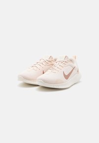 Light pink athletic shoes with a breathable mesh upper, white laces, and a contrasting brown Nike swoosh. Thick white soles and subtle texture.
