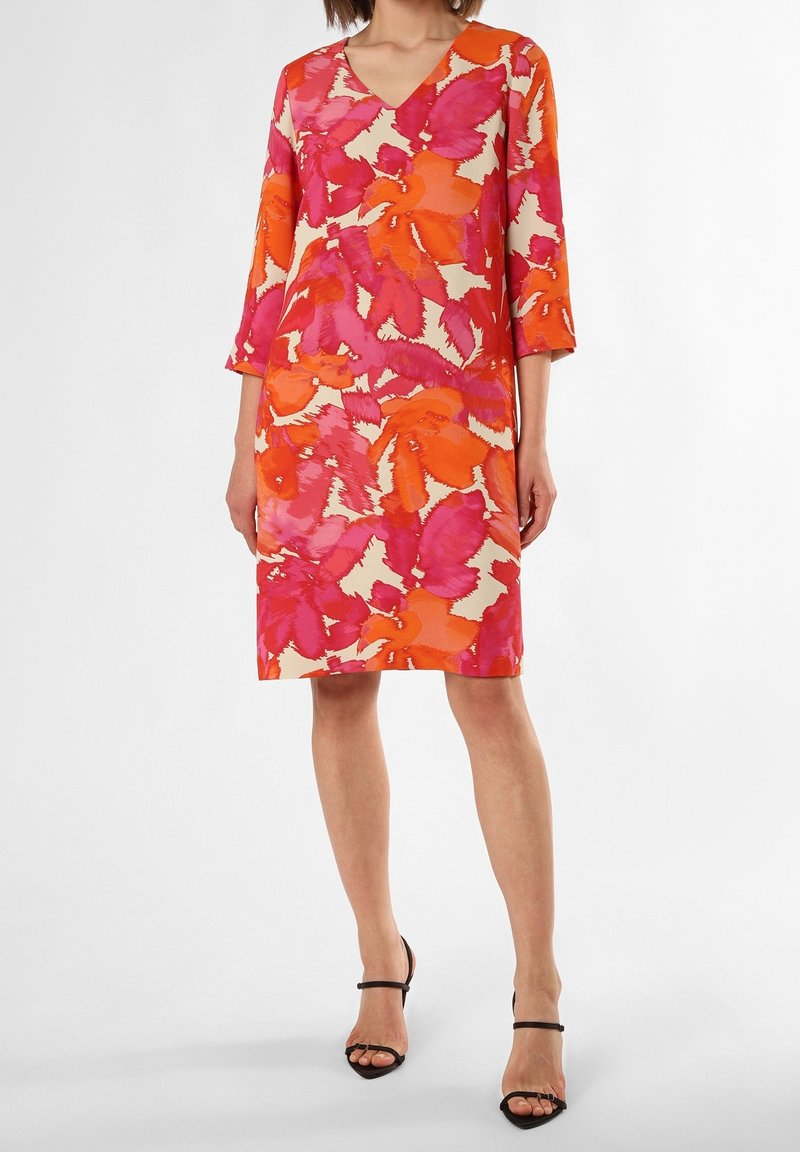 Robe florale avec un décolleté en V, des manches 3/4 et un motif abstrait dans des couleurs vives de rose, orange et crème. Texture du tissu lisse.