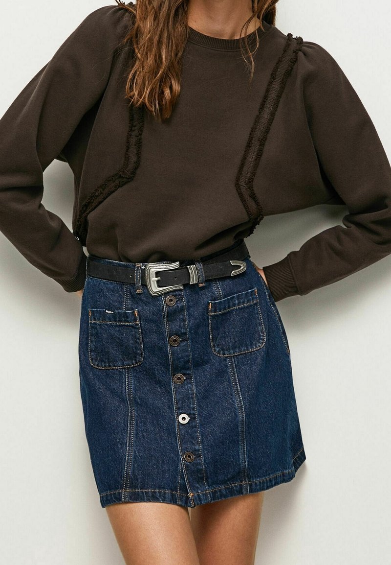 Sudadera marrón con detalles de ribete texturizado combinada con una falda de mezclilla azul claro que presenta un cierre de botones en la parte delantera y dos grandes bolsillos. Cinturón negro incluido.