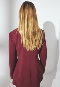 Bordo švarkas su struktūruotomis pečių siūlėmis ir pritaikytu siluetu, turintis lygią tekstūrą ir galinės siūlės detalizavimą, matomas iš nugaros.