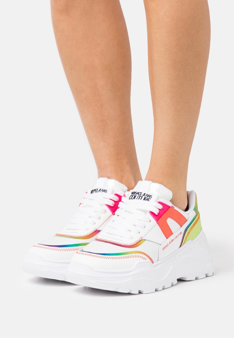 White sneakers with multicolored accents in pink, orange, and green. Designed with a chunky sole, textured panels, and contrasting stitching.