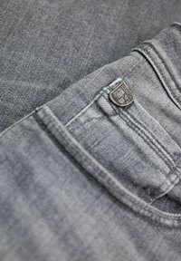 Jeans de mezclilla gris con un acabado texturizado y una pequeña etiqueta de logo plateado en el bolsillo trasero, con detalles de costura y un ajuste clásico.