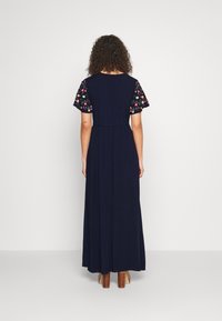 Marinblå maxiklänning med korta ärmar och färgglad blommig broderi. Slätt tyg och insydd midja ger en svävande siluett.