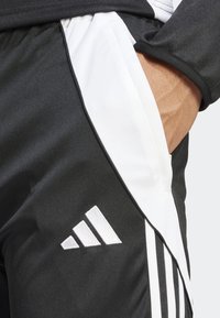Shorts sportivi neri con un pannello laterale bianco, righe verticali bianche e un logo ricamato bianco nella parte inferiore della gamba sinistra.