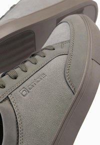 Šedé semišové tenisky s zaoblenou špičkou, texturovaným povrchem, plochými tkaničkami a nenápadným logem. Silná gumová podrážka s horizontálními drážkami.