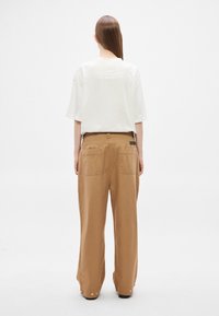 Luźna biała koszulka z wypukłym napisem na plecach, zestawiona z beżowymi, szerokimi spodniami z dwoma tylnymi kieszeniami i metalowymi guzikami.