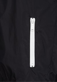 Giacca nera con cerniera bianca, caratterizzata da una superficie liscia e opaca e un design snello. La cerniera è posizionata centralmente e funzionale.