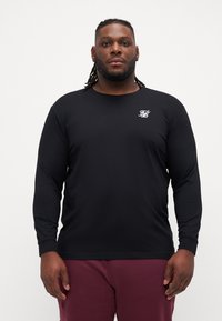 Long-sleeve black t-shirt made of lightweight fabric, featuring a small white logo on the chest. Smooth texture with a round neckline.