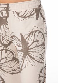 Baumwollhose mit einem großen, abstrakten Schmetterlingsmuster in Braun auf hellem Beigeton. Elastischer Bund und glatte Textur.