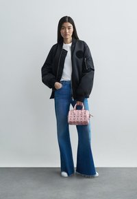 Veste bomber noire avec un patch rond, t-shirt blanc, jeans en denim bleu évasés et un petit sac à main rose clair avec des motifs de logo.