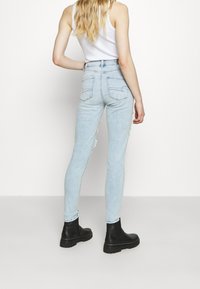 Ljust blå högmidjade skinny jeans med slitningar, fem fickor och sydda sömmar, tillsammans med svarta ankelskor.
