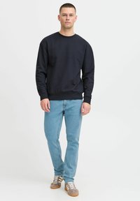 Sudadera navy con cuello redondo y puños acanalados, combinada con jeans de color azul claro y zapatillas grises con acentos en beige.