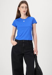 T-shirt aderente blu a maniche corte con collo rotondo e dettagli con logo, abbinato a pantaloni in denim neri a vita alta e una borsa nera texturizzata.