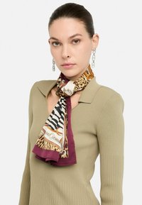 Pañuelo de seda con estampados de animales en tonos marrones y negros, con un borde burdeos. Estilizado de forma que se asemeja a una corbata.