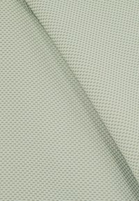 Texturovaná látka v bledě zelené barvě, zdobená malým, propracovaným diamantovým vzorem. Materiál se zdá být hladký a pevně tkaný.