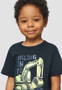 Donkerblauwe katoenen T-shirt met een grafisch ontwerp van een gele graafmachine, met de tekst "ROLLING IN TO..." afgedrukt in verschillende lettertypen. Ronde hals ontwerp.