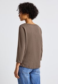 Braunes Longsleeve-Oberteil mit lockerer Passform und rundem Ausschnitt, kombiniert mit hellblauen Jeans. Glattes Material ohne Muster oder Akzente.