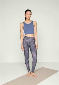 Blauer gerippter Cropped-Top, kombiniert mit gemusterten Leggings in lila- und grauverlauf, mit glatter Textur und hohem Taillendesign.