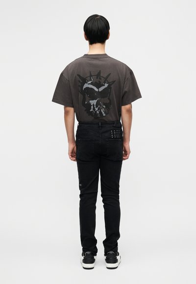 Liiga suur hallast puuvillast T-särk musta kolju graafikuga seljal, millele on lisatud mustad kitsad teksad ja mustad tossud.