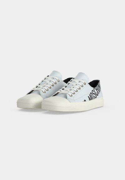 Paire de baskets basses blanches avec lacets et grand marquage texte noir sur le côté extérieur, présentée sur un fond clair uni.