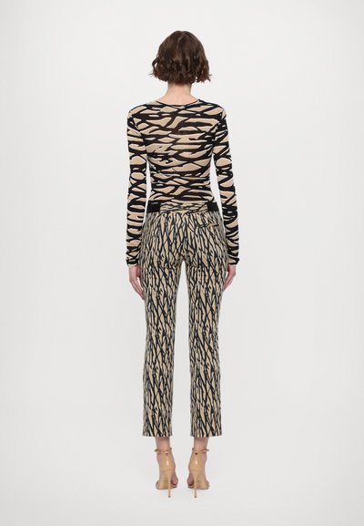 Long-sleeve top in beige and black pattern, paired with beige trousers featuring an abstract black line design, worn with transparent heeled shoes.