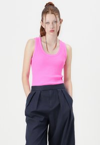 Enganliegendes, geripptes Tanktop in leuchtendem Pink mit rundem Ausschnitt. Kombiniert mit locker sitzenden, dunkelblauen Hosen mit gefalteter Vorderseite.