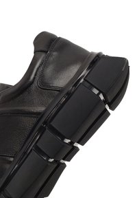 Baskets noires en cuir lisse avec une semelle en caoutchouc épaisse et segmentée, présentant un design texturé et des accents blancs contrastants.