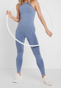 Jasnoniebieski sportowy top bez rękawów i legginsy, charakteryzujące się gładką teksturą i dopasowanym krojem. Modelka trzyma biały hula hoop na jednolitym tle.