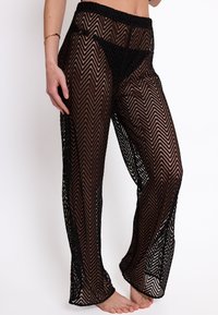Pantaloni neri in maglia trasparente con motivo a zigzag, dotati di vita elastica; vestibilità ampia e design a lunghezza totale; la texture appare delicata e leggera.