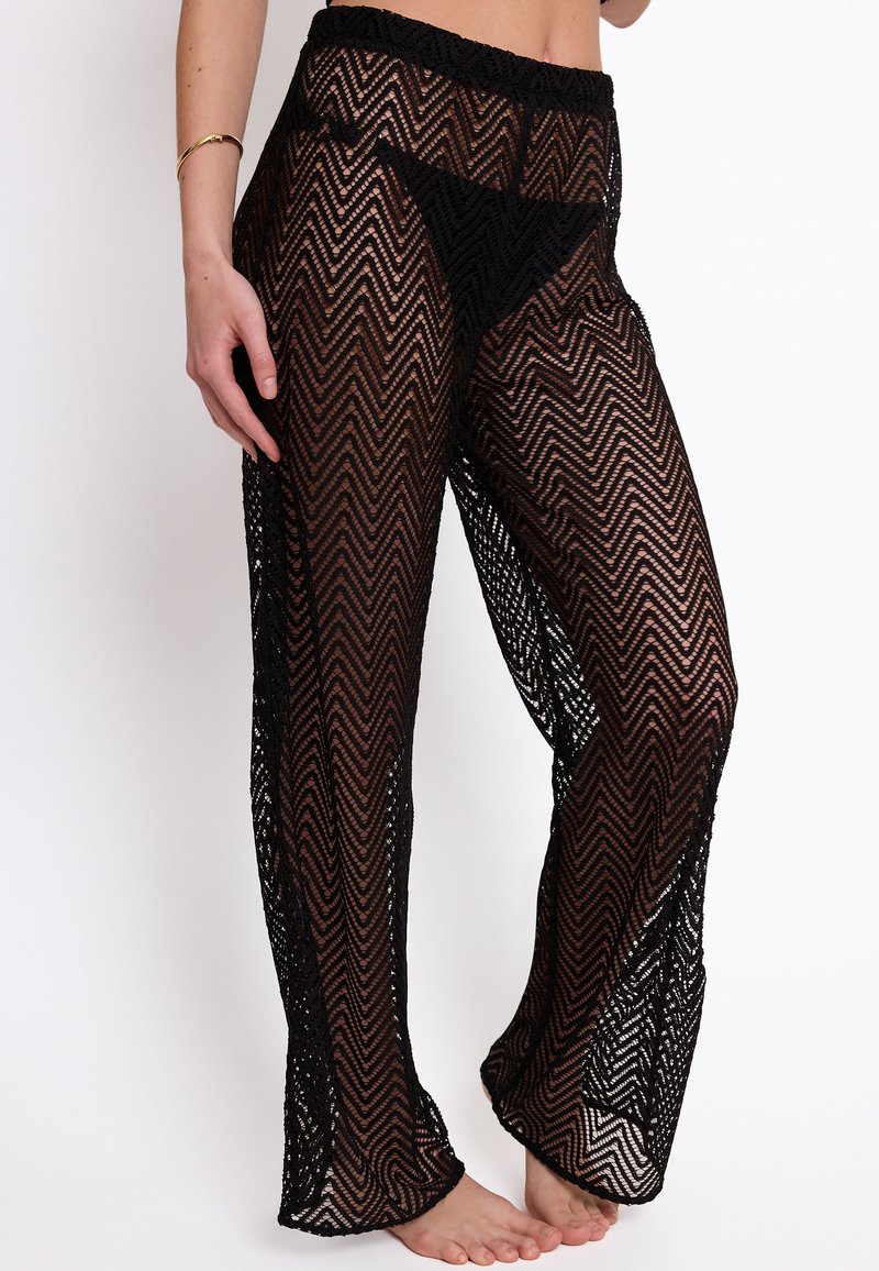 Pantaloni neri in maglia trasparente con motivo a zigzag, dotati di vita elastica; vestibilità ampia e design a lunghezza totale; la texture appare delicata e leggera.