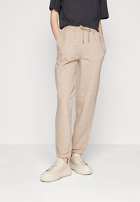 Beżowe spodnie dresowe z elastycznym pasem i sznurkiem do regulacji, zakończone ściągaczami przy kostkach. Zestawione z jasnymi trampkami. Prosty, luźny fason.