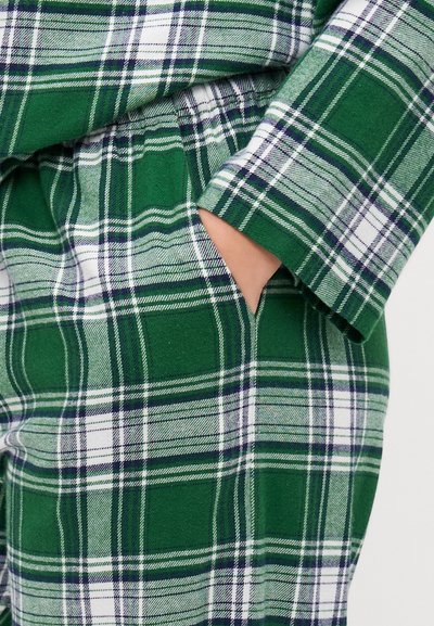Green plaid flannel fabric featuring a mix of dark green, white, and navy lines, with a pocket visible on the side and cuffed sleeves.
