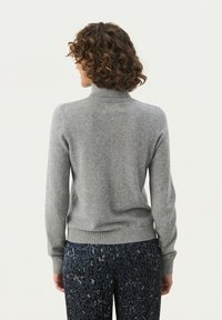 Grauer Rollkragenpullover aus weichem Material, mit gerippten Bündchen und Saum, kombiniert mit gemusterten Schlafanzughosen, von hinten betrachtet.