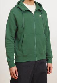 Grön zip-up hoodie med två framskott, dragsko på huvan, Nike-logotyp på bröstet, tillverkad av mjukt, texturerat tyg, och ribbade ärmslut och nederkant.