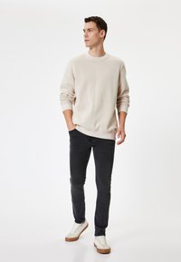 Sudadera beige claro con cuello redondo, puños acanalados y una costura en el frente; combinada con vaqueros ajustados negros y zapatillas blancas con suelas marrones.
