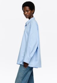 Lichtblauw overhemd met knoopsluiting, kraag en lange mouwen, gemaakt van een gladde stof. Gecombineerd met hoge blauwe jeans.
