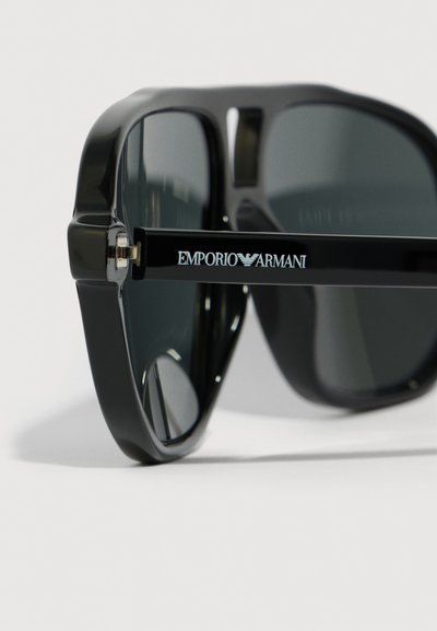 Černé plastové sluneční brýle s tmavými skly, s lesklým povrchem a logem Emporio Armani na nožičce pro branding.