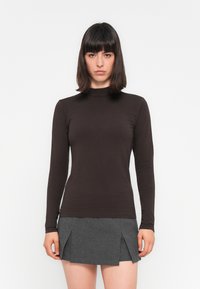 Langsleeve bruin top van gladde stof met een hoge halslijn, gecombineerd met een grijze mini-jurk met geplooide accenten.