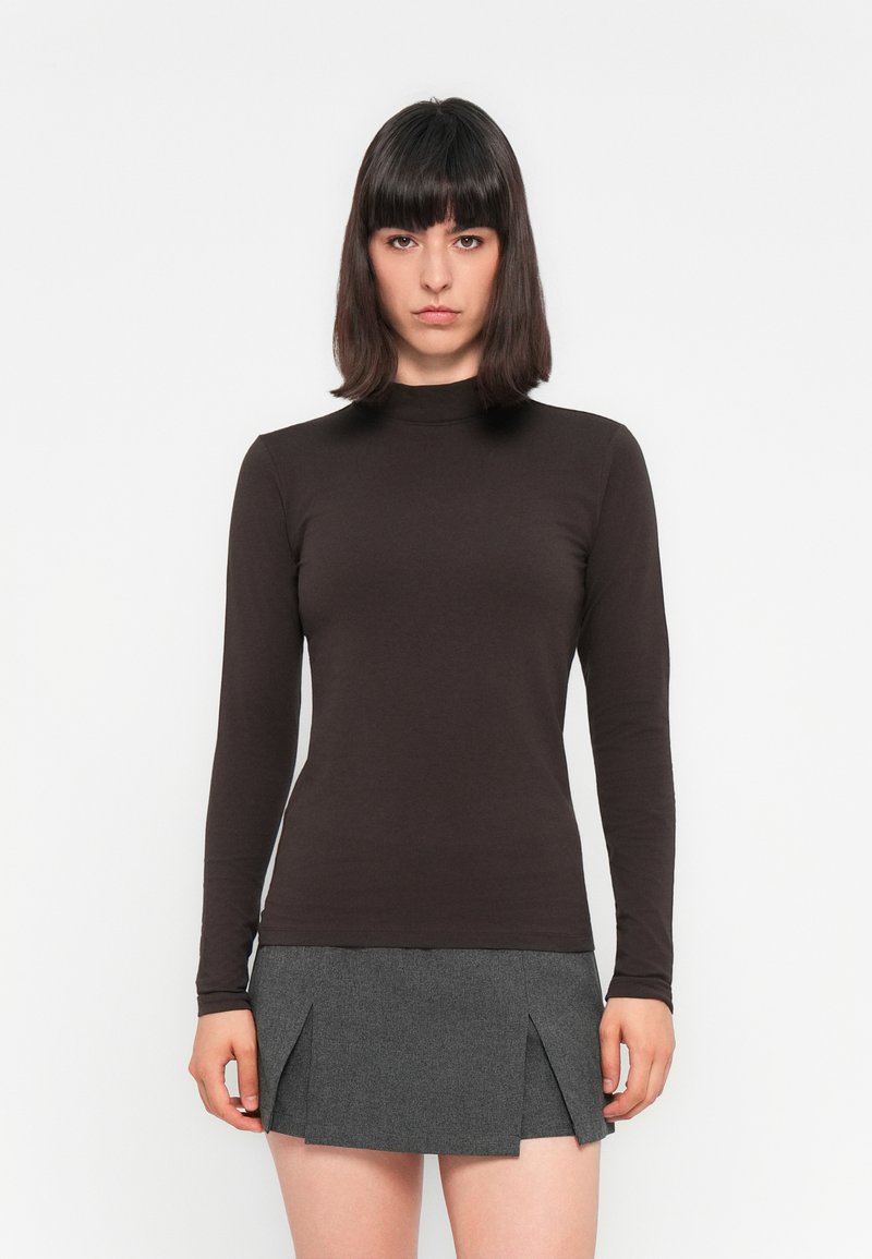 Langsleeve bruin top van gladde stof met een hoge halslijn, gecombineerd met een grijze mini-jurk met geplooide accenten.