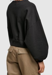 Black oversized sweatshirt with dropped shoulders and ribbed hem, paired with beige cargo pants featuring pocket flaps. Soft texture.