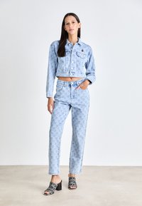 Chaqueta de mezclilla de corte crop azul claro y jeans de pierna recta, con un patrón sutil. Sandalias de piscina gráficas negras con tacón cuadrado.