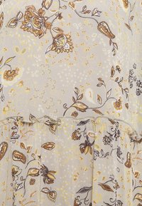 Tejido gris claro con patrones florales y de paisley en tonos amarillos, marrones y negros. El diseño tiene una apariencia suave y texturizada.