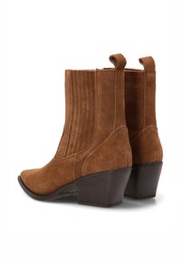 Botas de tobillo de ante marrón con punta cuadrada, paneles laterales texturizados y un tacón bajo y apilado. Cuenta con dos tiradores dobles para ponérselas fácilmente.